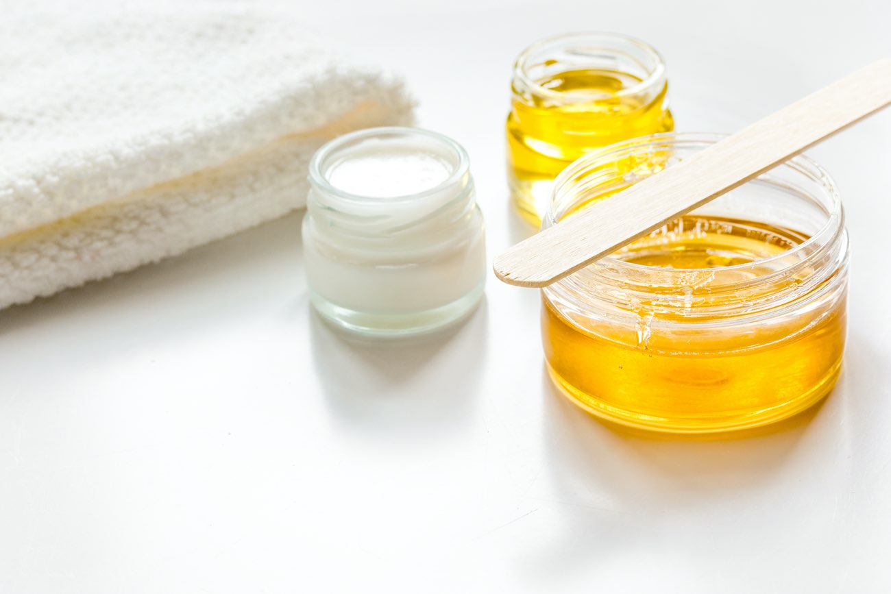 Immagine che mostra vari contenitori di prodotti per la cura della pelle, tra cui creme e oli, accanto a un asciugamano bianco. Ideale per suggerimenti di bellezza.