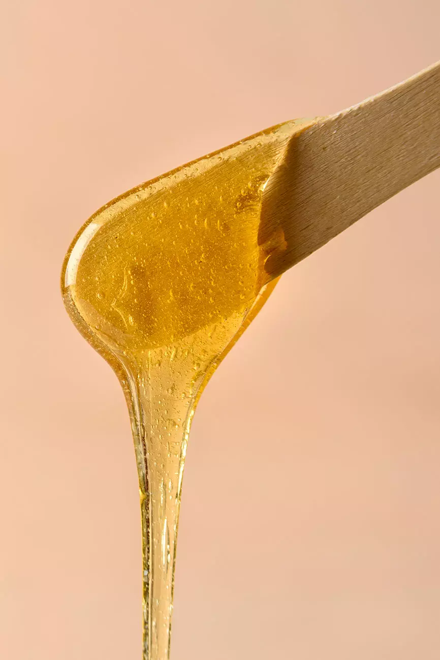 Una consistenza densa di cera dorata che gocciola da un bastoncino di legno su uno sfondo neutro. 
