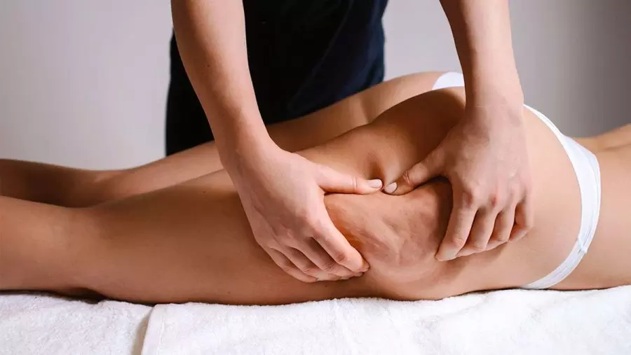 Un massaggiatore applica tecniche di rilassamento sulla coscia di un cliente durante un trattamento benessere, evidenziando la cura per il corpo.