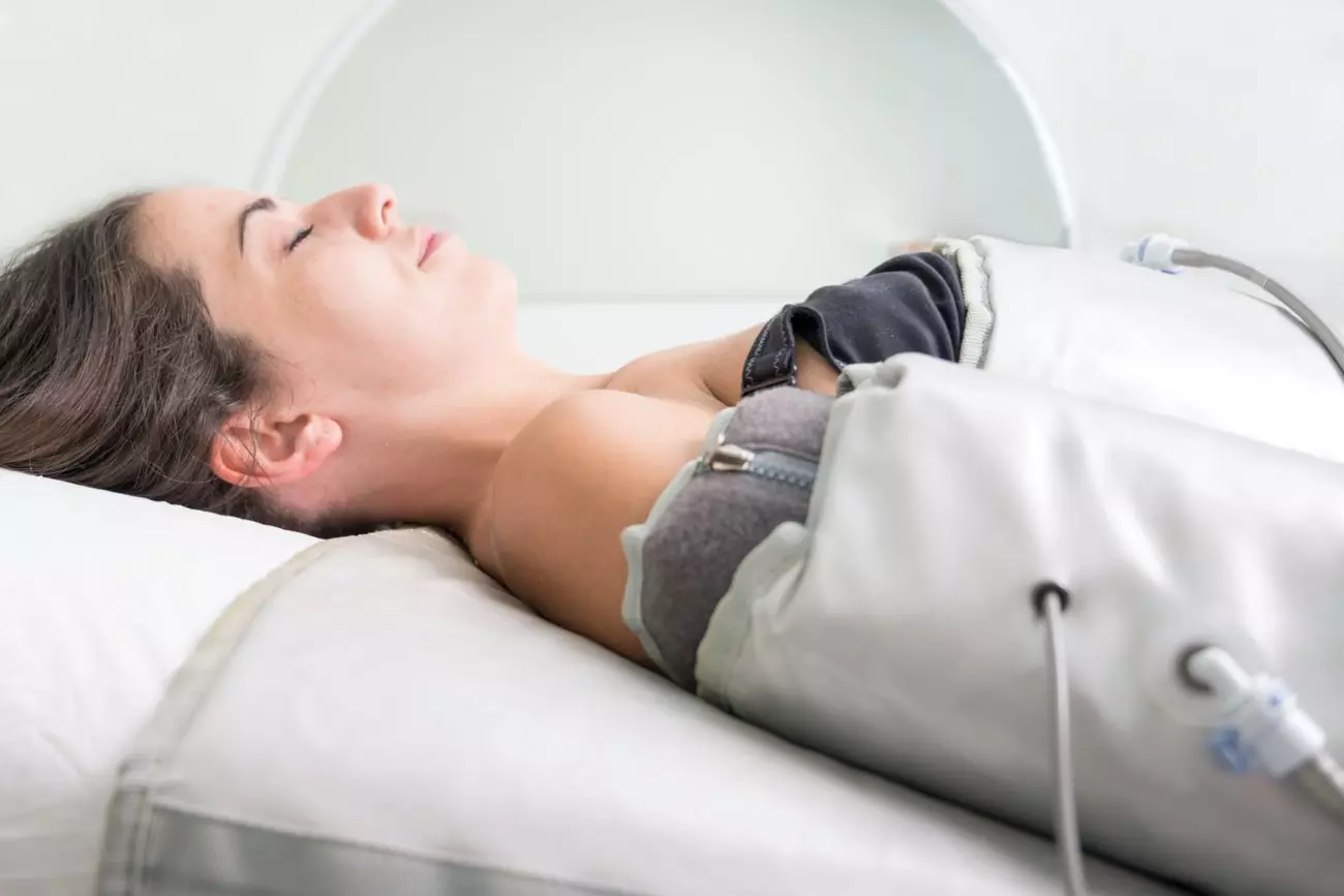 Una giovane donna distesa su un letto mentre riceve un trattamento terapeutico con dispositivi pneumatici, rilassata e con gli occhi chiusi.